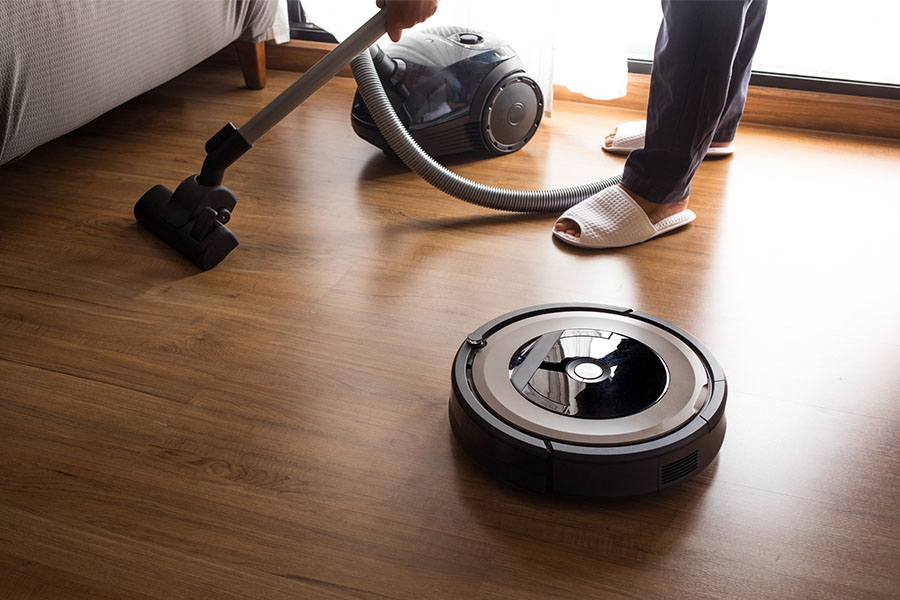 Robot vacuum cleaner with a person using a normal vacuum behind it