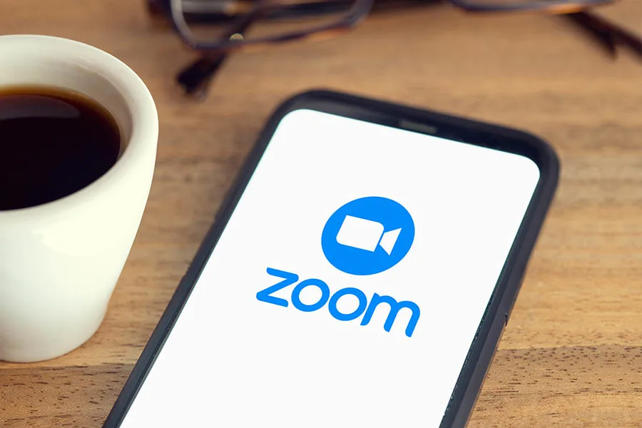 iphone on desk with Zoom video conferencing app logo on screen.