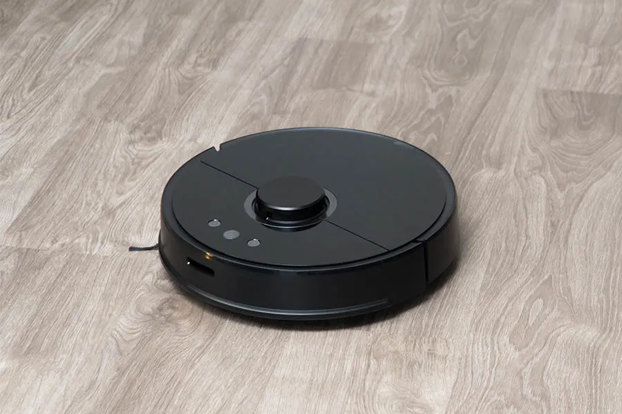 Robot vacuum cleaner black on the floor is cleaning, gray laminate