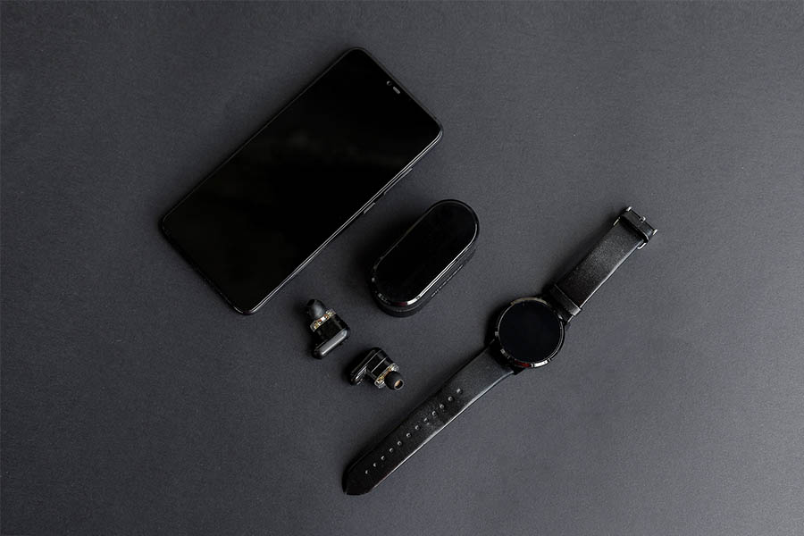 Black pen, black smart watch, smartphone, wireless headphones on dark background