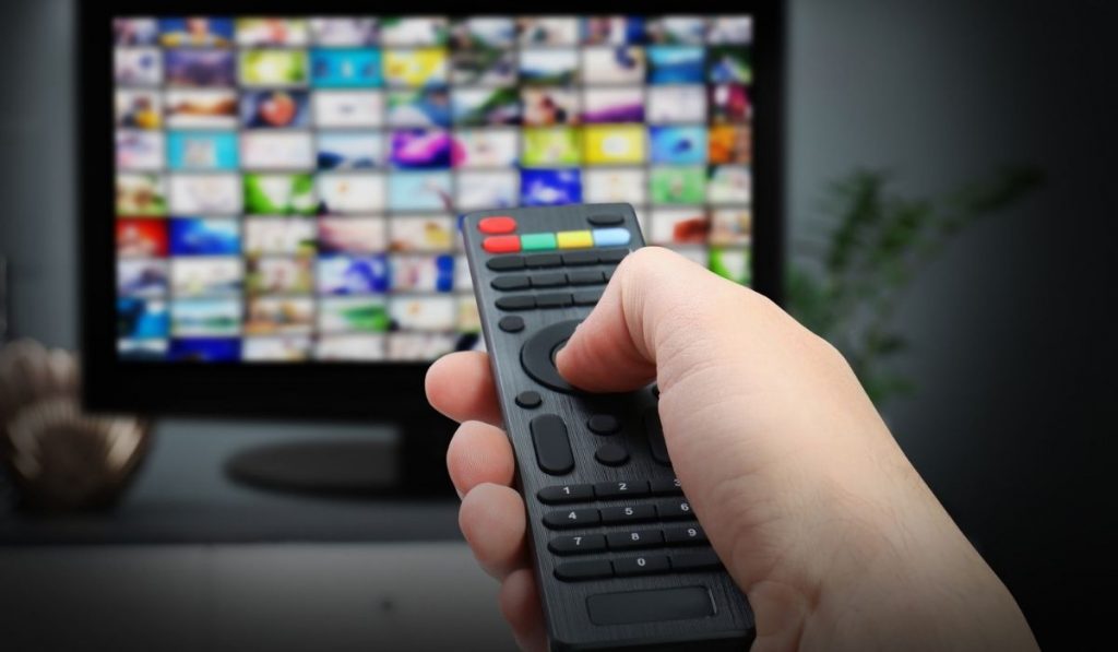 Woman using remote control to change channels on TV