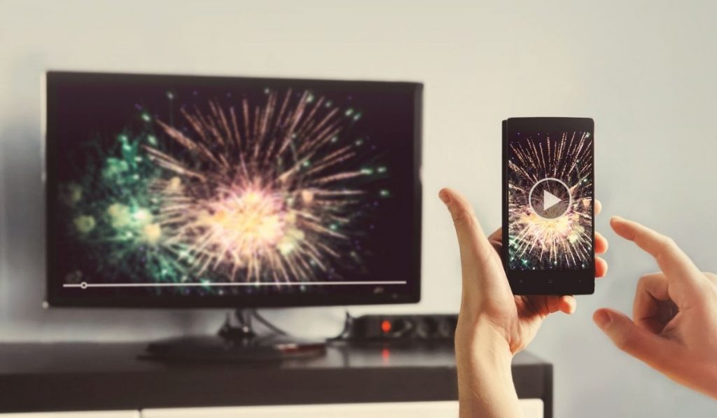 Man With Smartphone Connected To A TV Watching Video At Home