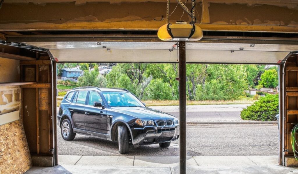 Black Suv turning into garage with automatic overhead door opener - grainy unfinished surfaces and pavement