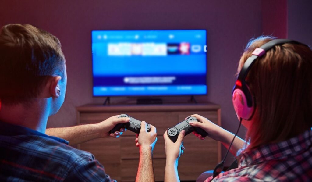 Gamers enjoying Playing Video Games on Playstation indoors sitting on the sofa, holding Console 