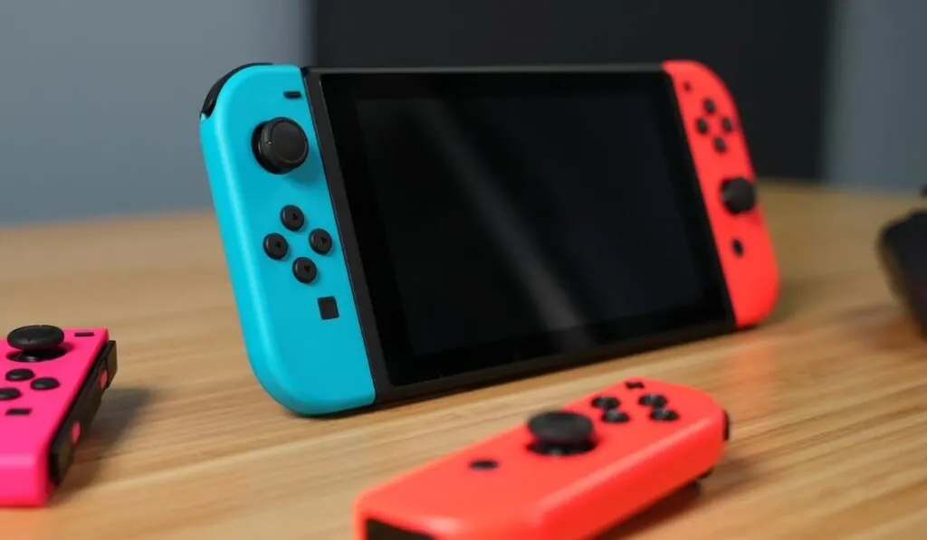 Nintendo Switch, 2 joycons, and controller on a wooden desk - 2