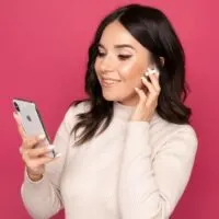 Young woman using airpods to listen to music isolated on the pink background