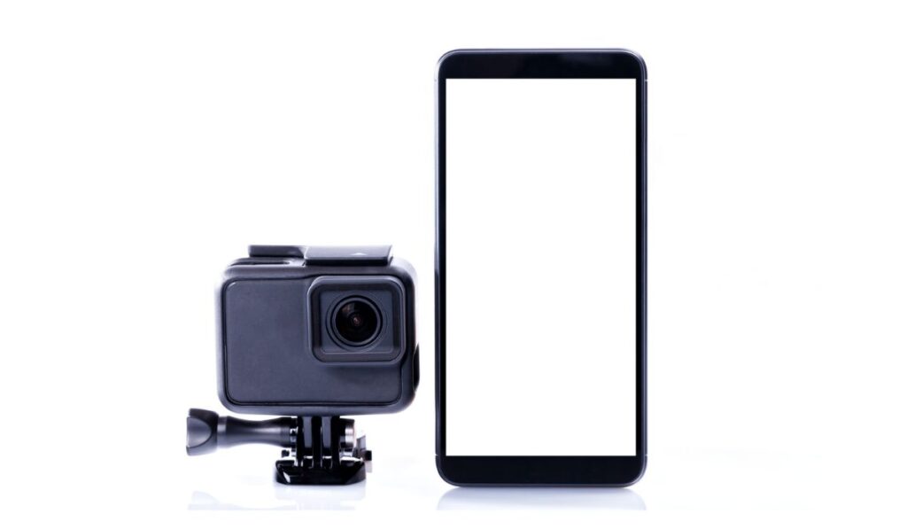 Современная видеокамера рядом с черным смартфоном с изолированным экраном