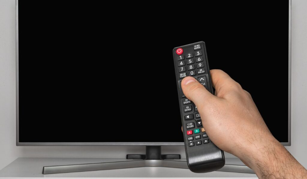 Черный экран на телевизоре и человеческая рука с пультом дистанционного управления телевизором