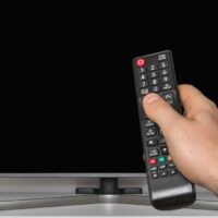 Black screen on TV and human hand with TV remote control