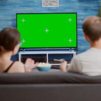 Couple sitting on couch watching television on green screen flat tv