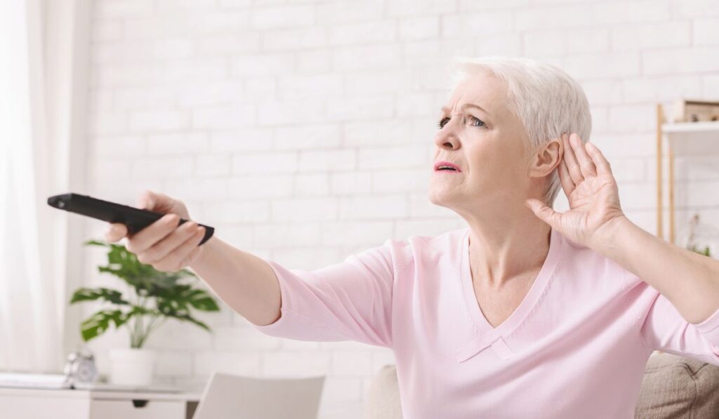 Elderly woman rising tv set volume with remote control