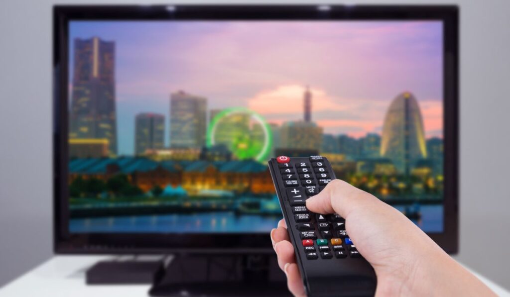 Hand holding TV remote control with a television and city screen