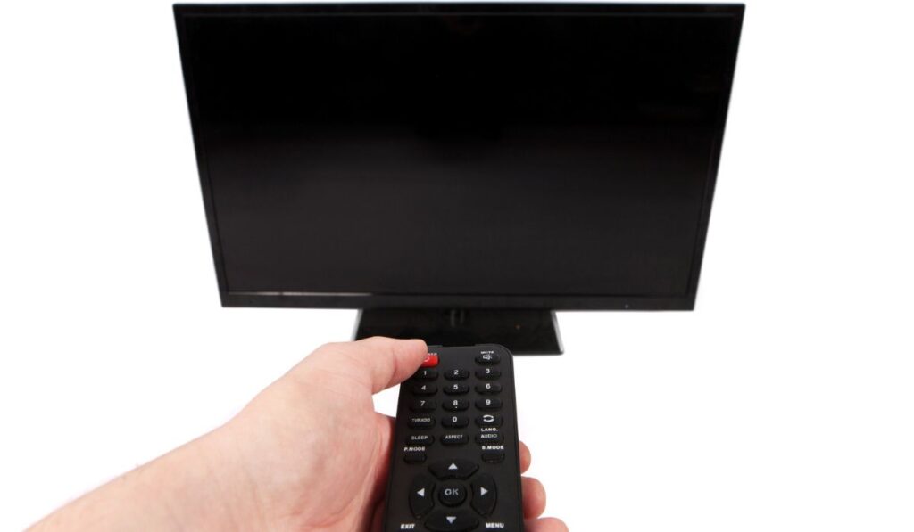 Рука с помощью пульта дистанционного управления перед телевизором с пустым черным sc
