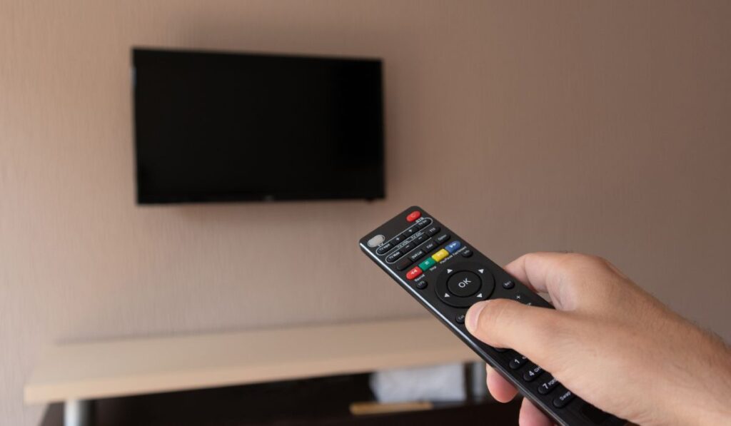 Male hand with tv remote control and blurred television with a black screen