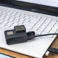 Mock up of a smartphone and an action camera connected to a white laptop on a wooden table background