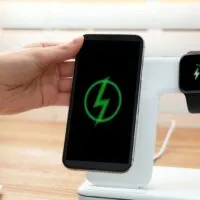 Woman putting mobile phone onto wireless charger at table