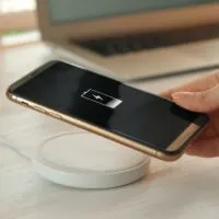 Woman putting mobile phone onto wireless charger at wooden table