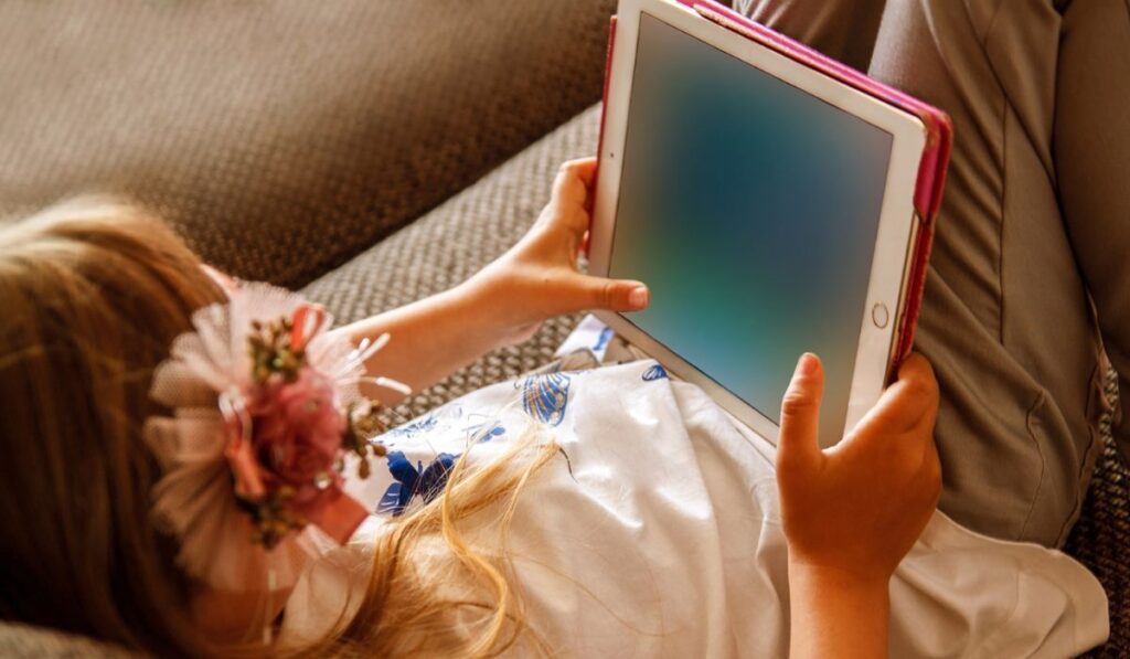 Cute girl kid using iPad digital computer tablet on bed for education or playing game 