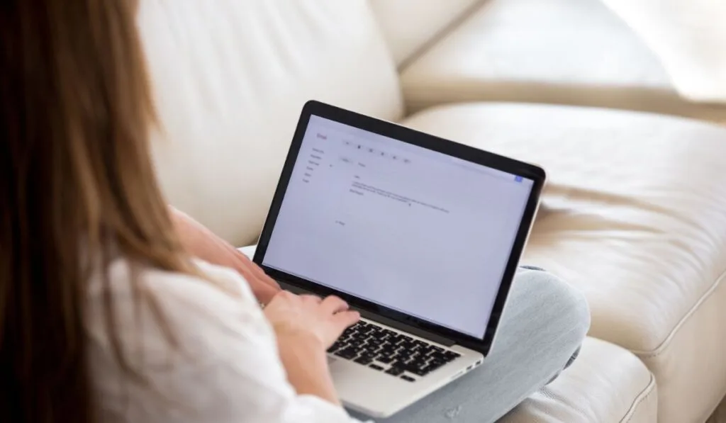 Rear view at woman writing email on laptop at home