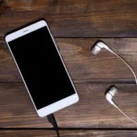 White mobile phone on a wooden wooden background with headphones charging cable