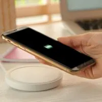 Woman putting mobile phone onto wireless charger at white wooden table
