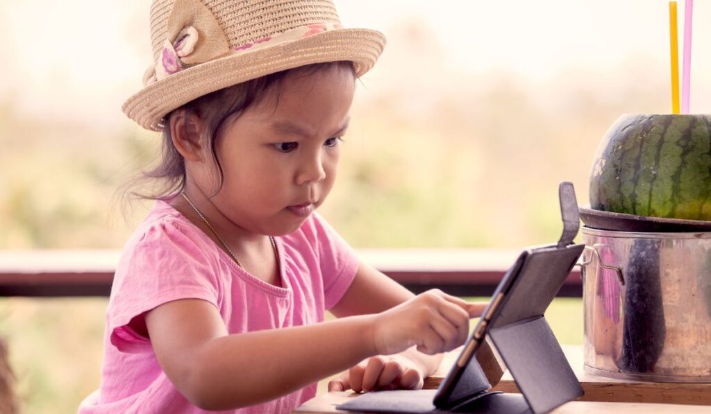Азиатская маленькая девочка играет в планшет ipad 