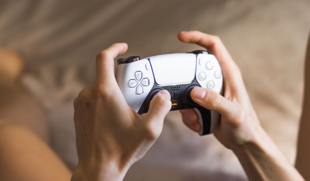 Держа контроллер Play Station 5 Dual Sense и играя в видеоигры дома 