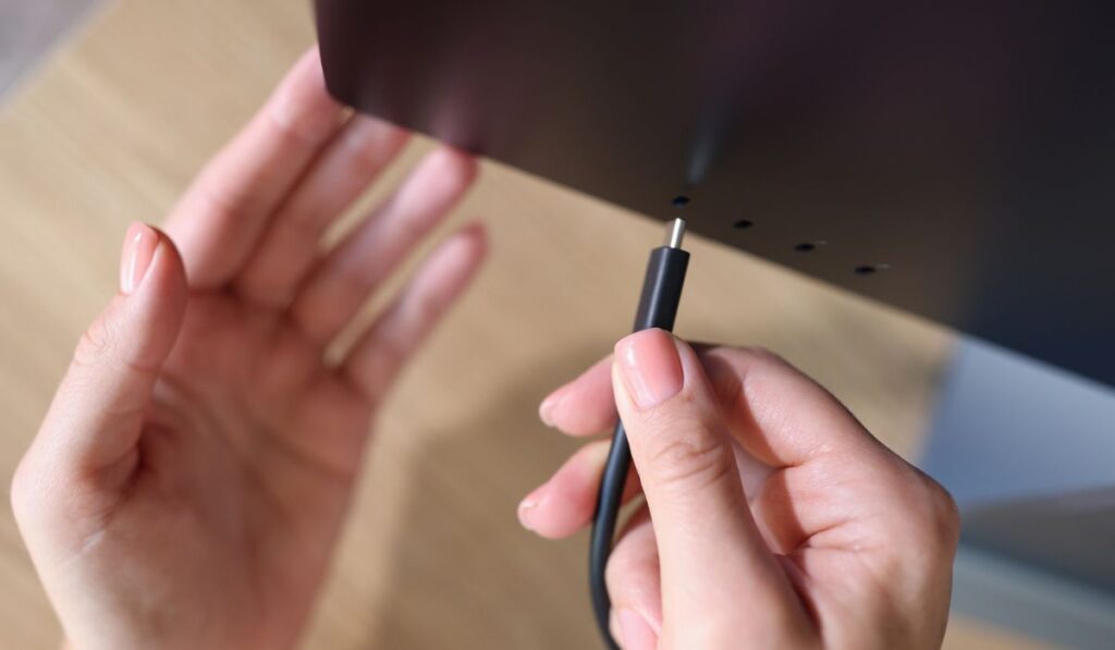 Person hand connects a black USB-C or Type C power cable to computer