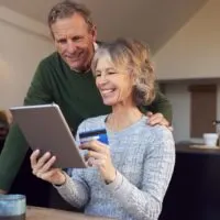 Retired Senior Couple At Home Buying Products Or Services Online With Digital Tablet And Credit Card
