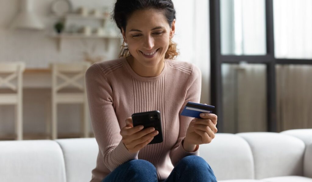 Smiling latina lady holding phone bank card make online shopping 