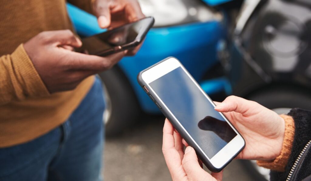 Крупный план двух автомобилистов, обменивающихся страховыми данными на мобильном телефоне после автокатастрофы