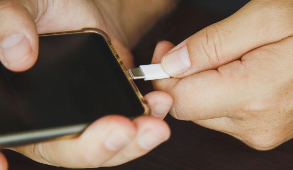 Закройте руки человека с помощью кабеля USB типа C для зарядки мобильного телефона на деревянном столе