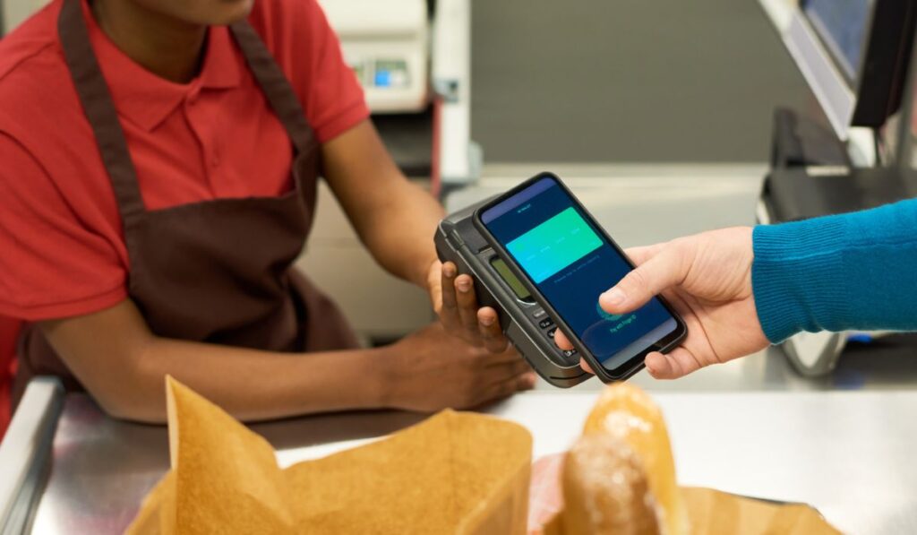 Рука потребителя со смартфоном, оплачивающего продукты питания бесконтактным платежом