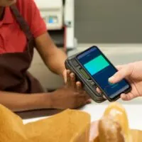 Hand of consumer with smartphone paying for food products by contactless payment