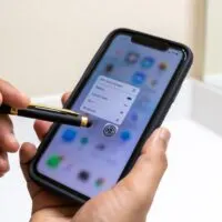 Man uses a stylus pen to click the settings app on a cell phone