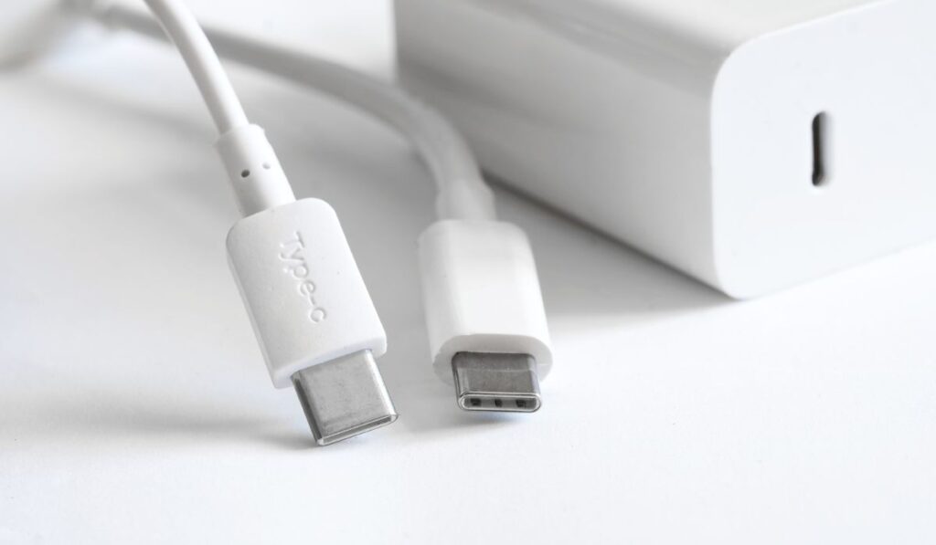Two white usb type-c connectors with wires lie on a light background next to a white power supply and fast charger 