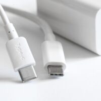 Two white usb type-c connectors with wires lie on a light background next to a white power supply and fast charger