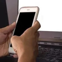 Hands that are touching a black screen phone to work online at home