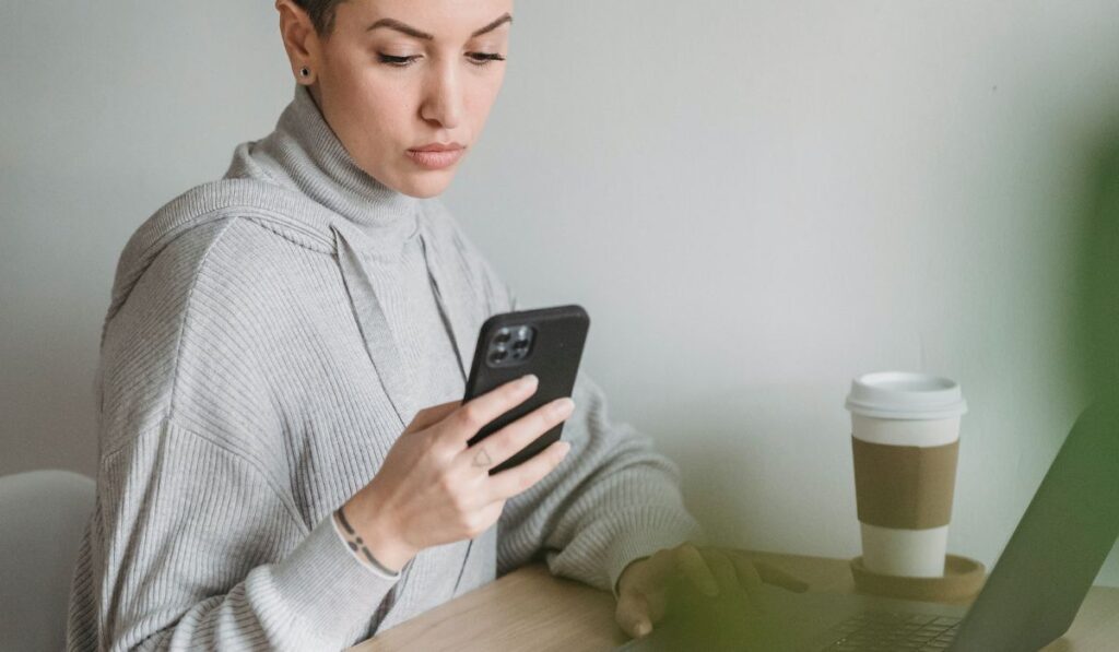 Сосредоточенная женщина, использующая смартфон и работающая на ноутбуке
