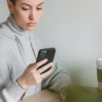 Focused woman using smartphone and working on laptop