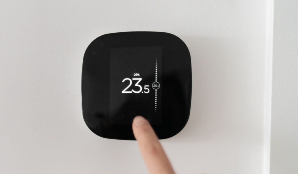 Smart home digital thermostat touch screen woman touching touchscreen to adjust temperature of heating in living room