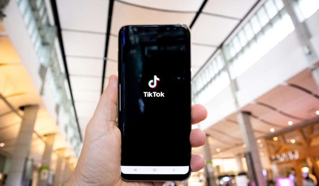 Рука человека, держащего мобильный телефон, открывает приложение TikTok