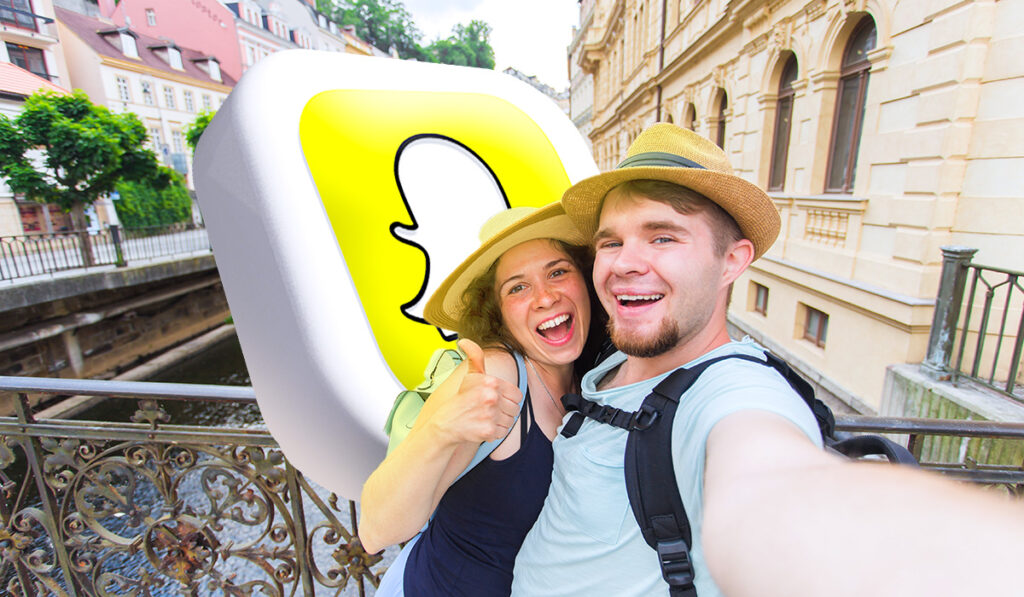 couple taking a selfie on a bridge with the snapchat logo behind them