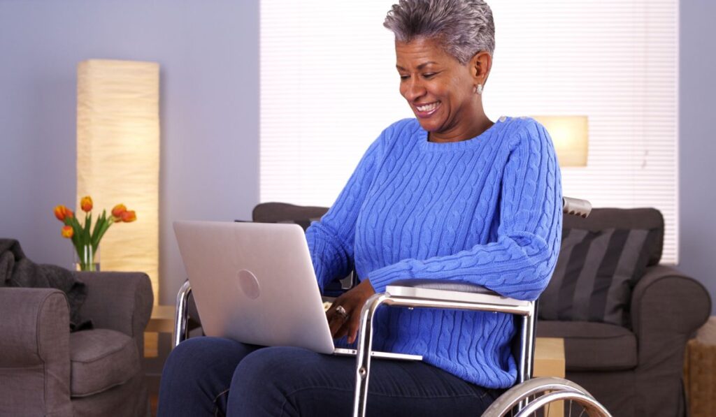 Зрелая черная женщина сидит в инвалидной коляске с ноутбуком