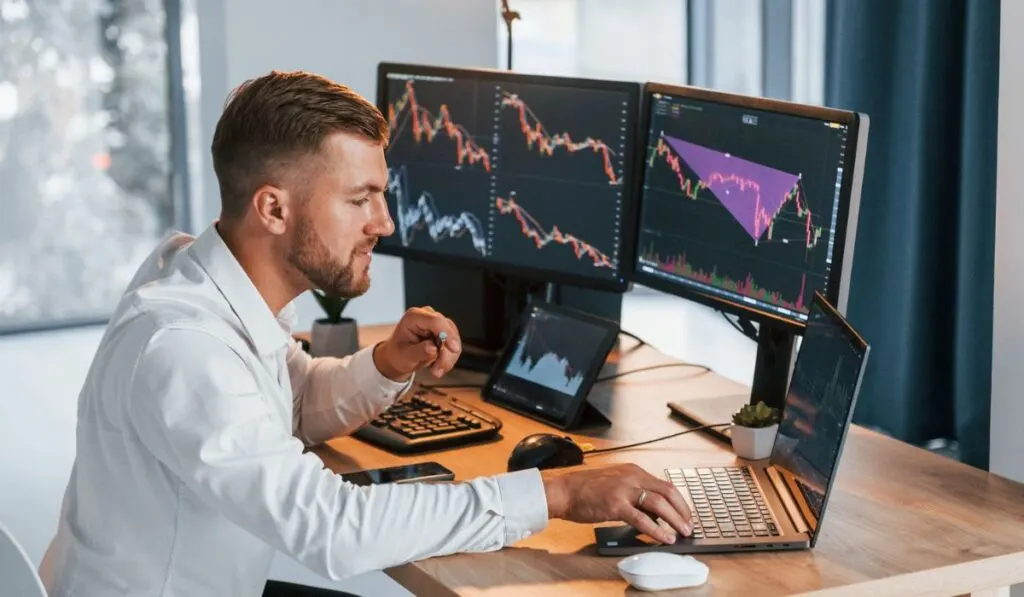 Young businessman in formal clothes is in office with multiple screens