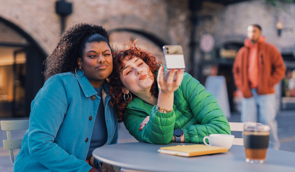 Two women taking a selfie at an outdoor table