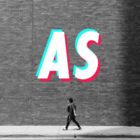 Black and white photo of a woman walking next to a brick building, the letters 'AS' shown above