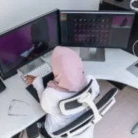 Female Arabic creative professional working at home office on desktop computer with dual screen monitor top view