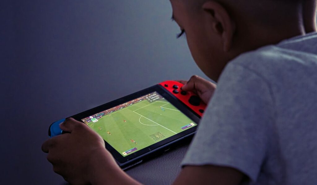 Мальчик играет на Nintendo Switch с футбольным полем на экране